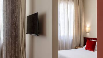 Une chambre d’hôtel avec un lit, un téléviseur fixé au mur, une chaise et une grande colonne.
