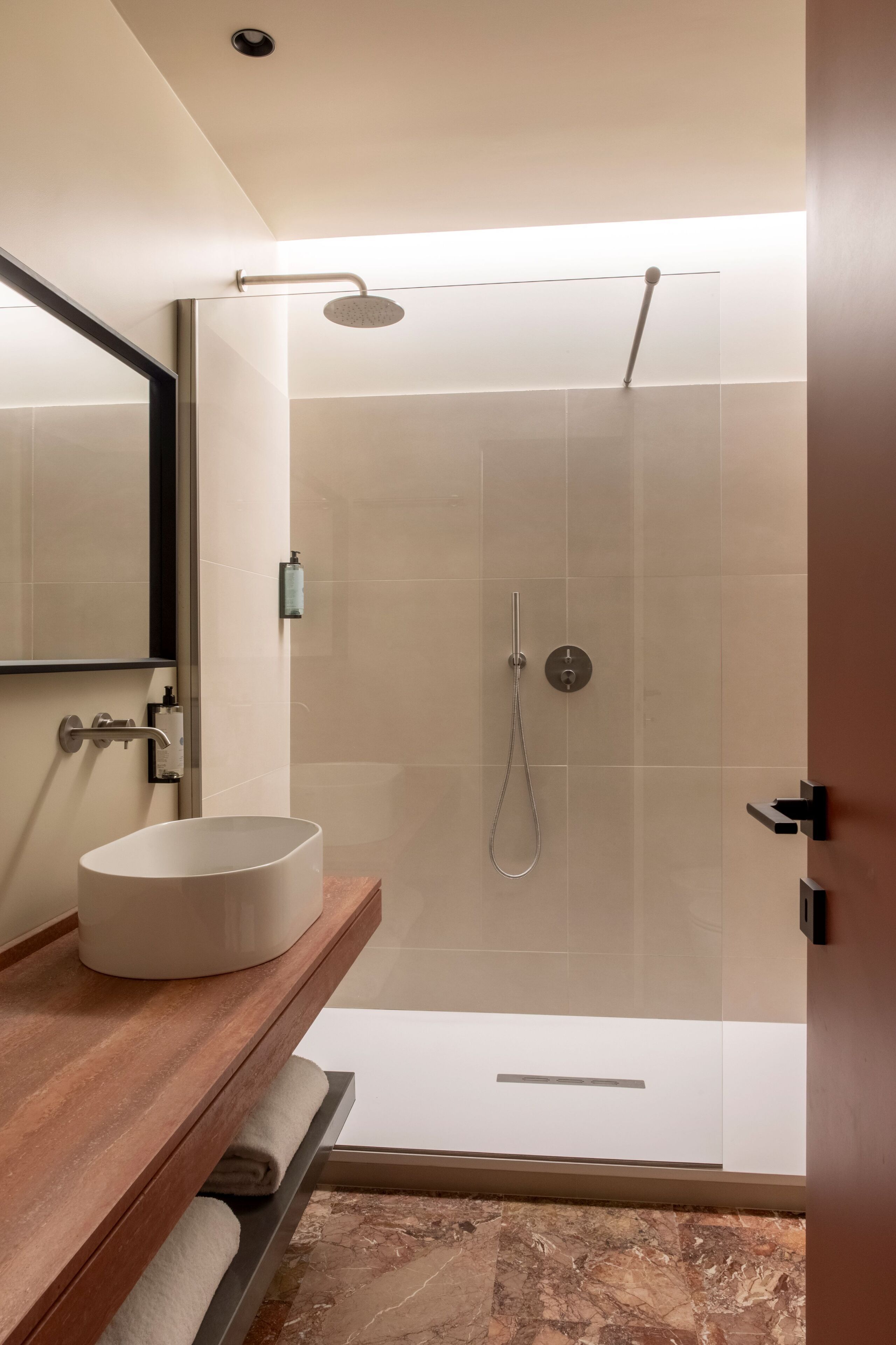 A modern bathroom with a glass-enclosed shower, a white sink, and a wooden vanity.