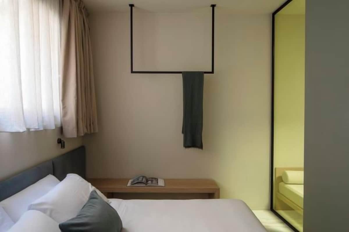 Ein Hotelzimmer mit Bett, Nachttisch mit Buch, aufgehängtem Handtuch und Fenster mit Blick.