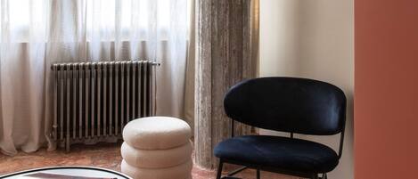 A room with a round table, a black chair, a tall column, and a radiator.