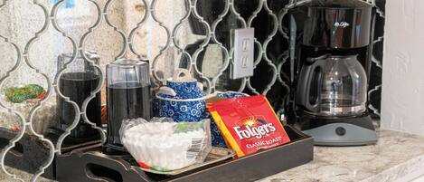 A kitchen counter with a coffee maker, a blue and white ceramic container, a bag of Folgers coffee, and a tray with utensils.