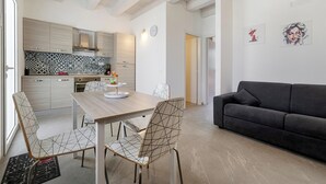 A modern kitchen with wooden cabinets, a tiled backsplash, and a dining area with a table and chairs. There is a black sofa in the living area. - The Red Apartment (Punta Secca)