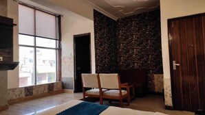 A room with a large window, a stone wall, a wooden door, and a chair. - Hotel Vistara Grand (Haridwar)