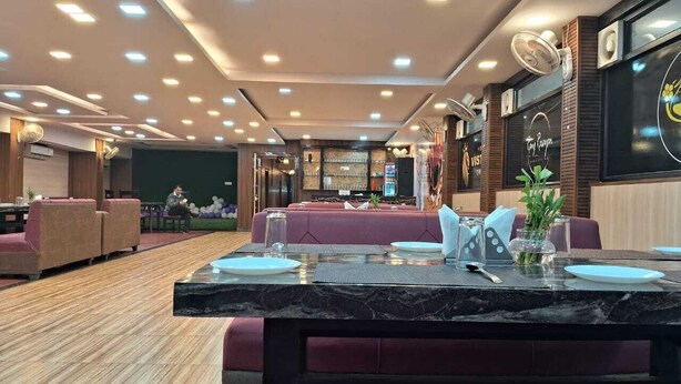 A modern restaurant with a marble table set for two, cushioned seating, and a well-lit ceiling with recessed lighting. - Hotel Vistara Grand (Haridwar)