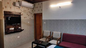 A living room with a flat-screen TV, two armchairs, a sofa, and a coffee table. - Hotel Vistara Grand (Haridwar)