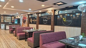 A restaurant with red cushioned booths, marble tables, and a modern ceiling design. - Hotel Vistara Grand (Haridwar)