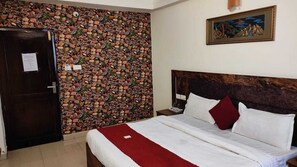 A bedroom with a bed, a wooden headboard, a nightstand, a red throw blanket, and a wall with a mosaic pattern. - Hotel Vistara Grand (Haridwar)