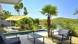 Zona de piscina con sillones reclinables, una mesa y vistas a un paisaje montañoso.