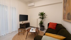 A living room with a flat-screen TV, a potted plant, a sofa with cushions, a coffee table, and a TV stand. - Acropolis Walk • Starlink • Sunset Rooftop (Athens)