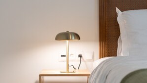 A neatly made bed with a wooden nightstand beside it, a lamp on the nightstand, and a power outlet. - Acropolis Walk • Starlink • Sunset Rooftop (Athens)