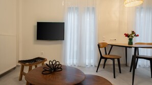 En moderne stue med et fladskærms-tv, et rundt træbord, to stole, en lille skammel og en vase med blomster.