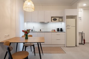 Une cuisine moderne avec des meubles blancs, un four à micro-ondes, un réfrigérateur, une table à manger avec des chaises et un luminaire suspendu.