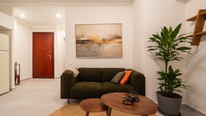 En stue med sofa, to små borde, en potteplante og et billede på væggen.
