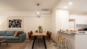 Un soggiorno moderno con un divano blu, un tavolo da pranzo in legno e una zona cucina con mobili bianchi e isola integrata.