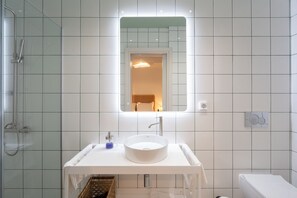 A modern bathroom with a white sink, a glass shower enclosure, and a mirror above the sink. - Bright Spacious 3BR/2BA near Acropolis | Rooftop (Athens)