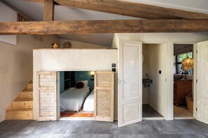 A room with a loft bed, a wooden staircase, and a view of a kitchen area.