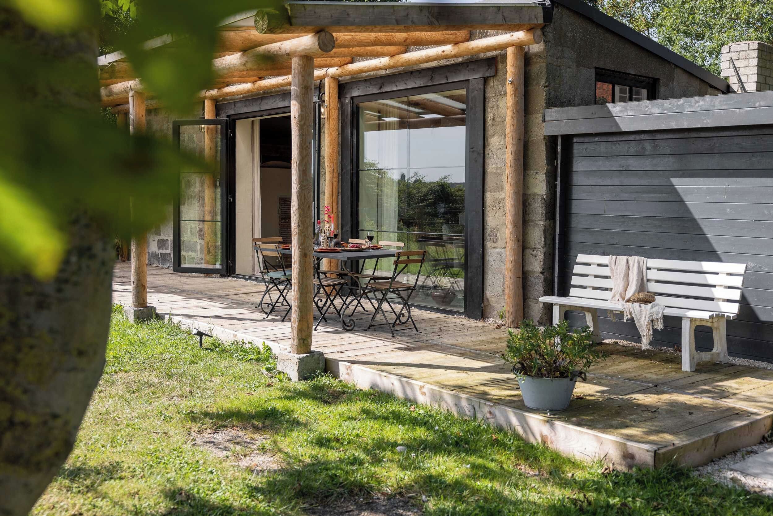 Un espace extérieur aménagé en bois, avec des tables et des chaises, un banc et un pot de fleurs.
