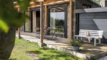 Un espace extérieur aménagé en bois, avec des tables et des chaises, un banc et un pot de fleurs.