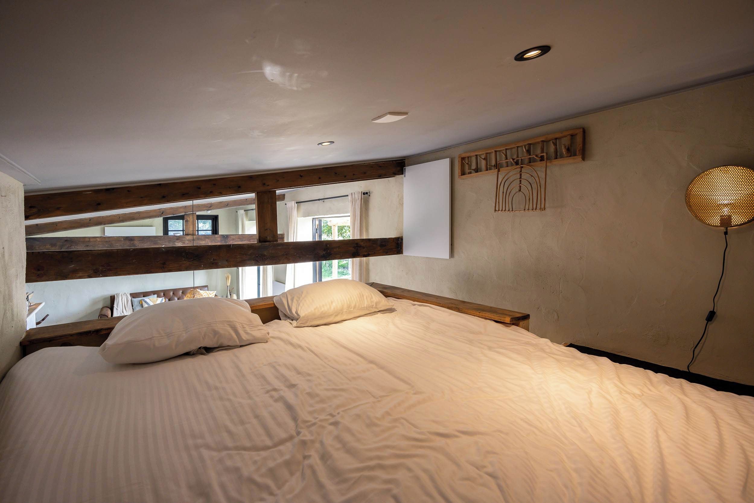 Een slaapkamer met een bed, houten balken, een wandlamp en een raam.