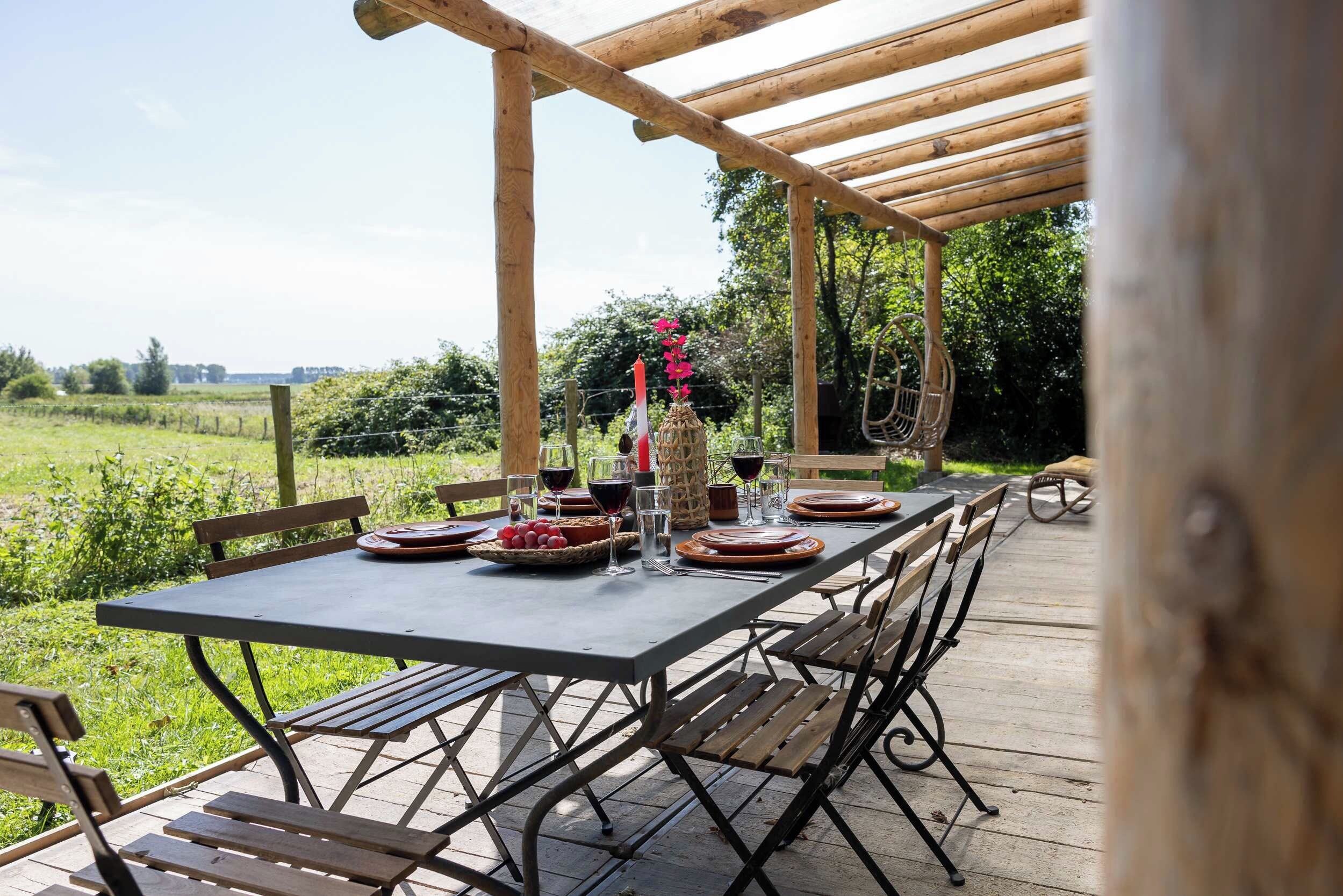 Een terras met een eettafel gedekt voor twee personen, omringd door houten stoelen en banken.