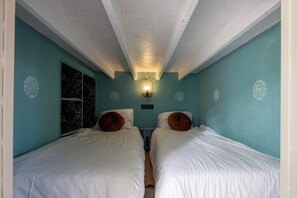 A room with two beds, a wall-mounted light fixture, and a window with a floral pattern.