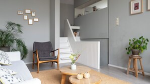 En moderne stue med sofa, lænestol, sofabord, trappe og en potteplante.