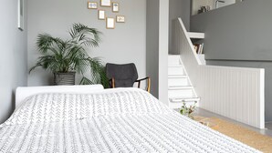 Et moderne soveværelse med en seng, en stol, en stor stueplante og en trappe.