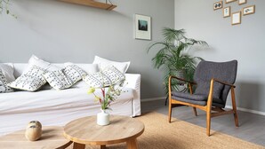 En moderne stue med en hvid sofa, puder med mønster, et rundt træbord, en grå lænestol og en potteplante.