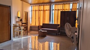 A modern living room with a sofa, a dining table with chairs, a small table with a vase and a clock, and a fan. - THE LUSHAI INN (Aizawl)