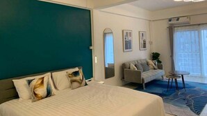 A hotel room with a bed, a sofa, a small table, and a large window with curtains. - Mana restaurant and boutique hotel (Khon Kaen)