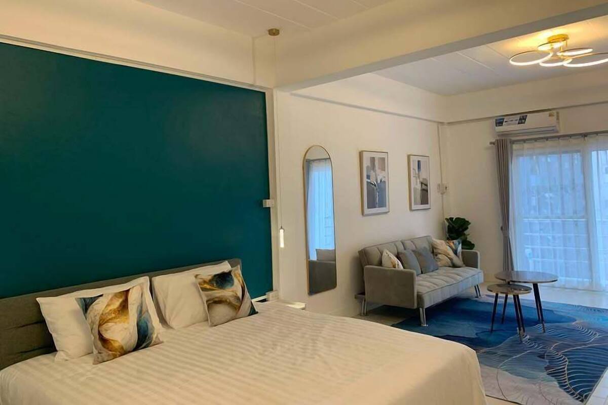 Una habitación de hotel con cama, sofá, una mesita y un amplio ventanal con cortinas.