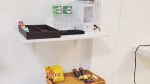 A small refrigerator with a basket of snacks and a microwave on a white shelf above it. - Mana restaurant and boutique hotel (Khon Kaen)