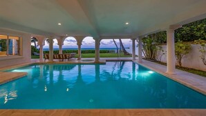 Une piscine intérieure avec vue sur l’océan, entourée de colonnes et abritée par une structure couverte.