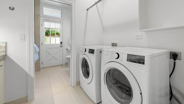 A laundry area with two front-loading washing machines, a door leading to a balcony, and a wall-mounted drying rack.