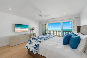 Ein Schlafzimmer mit einem Bett, einem Deckenventilator, einem Schreibtisch und Blick auf den Ozean durch eine Schiebetür.