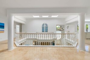 A spacious interior with a central staircase, white walls, and a large arched window.