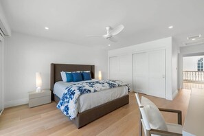 A bedroom with a bed, bedside tables, a ceiling fan, and a view of the outside.