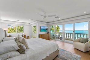A bedroom with a large bed, a ceiling fan, and a view of the ocean through sliding glass doors.