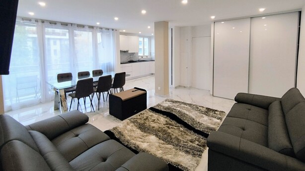 A modern living room with a sofa set, a dining table with chairs, and a kitchen area in the background. - L'Exclusif - Paris - Neuilly - Levallois (Levallois-Perret)