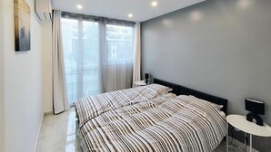 A modern bedroom with a large bed, a bedside table, and a window with curtains. - L'Exclusif - Paris - Neuilly - Levallois (Levallois-Perret)