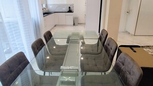A modern conference room with a glass table and cushioned chairs, a kitchen in the background, and large windows. - L'Exclusif - Paris - Neuilly - Levallois (Levallois-Perret)