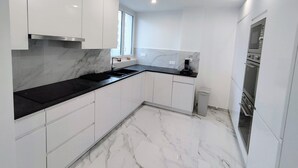 A modern kitchen with white cabinets, a black countertop, and a marble backsplash. - L'Exclusif - Paris - Neuilly - Levallois (Levallois-Perret)