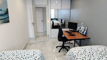 Una habitació d'hotel amb dos llits, un escriptori amb un ordinador i una petita zona de seients.