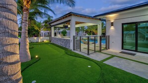 A modern house with a covered patio, a swimming pool, and a well-maintained lawn.