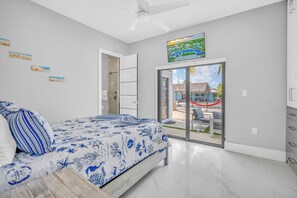 A bedroom with a bed, a ceiling fan, a sliding glass door leading to an outdoor area, and a painting above the door. - Paradise Oceanside Estate- 6 Bedrooms & 9 BR + Office + Theater Room – SLEEPS 14 (Marathon)
