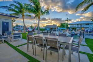A patio with a dining table and chairs, surrounded by palm trees and a pool area. - Paradise Oceanside Estate- 6 Bedrooms & 9 BR + Office + Theater Room – SLEEPS 14 (Marathon)