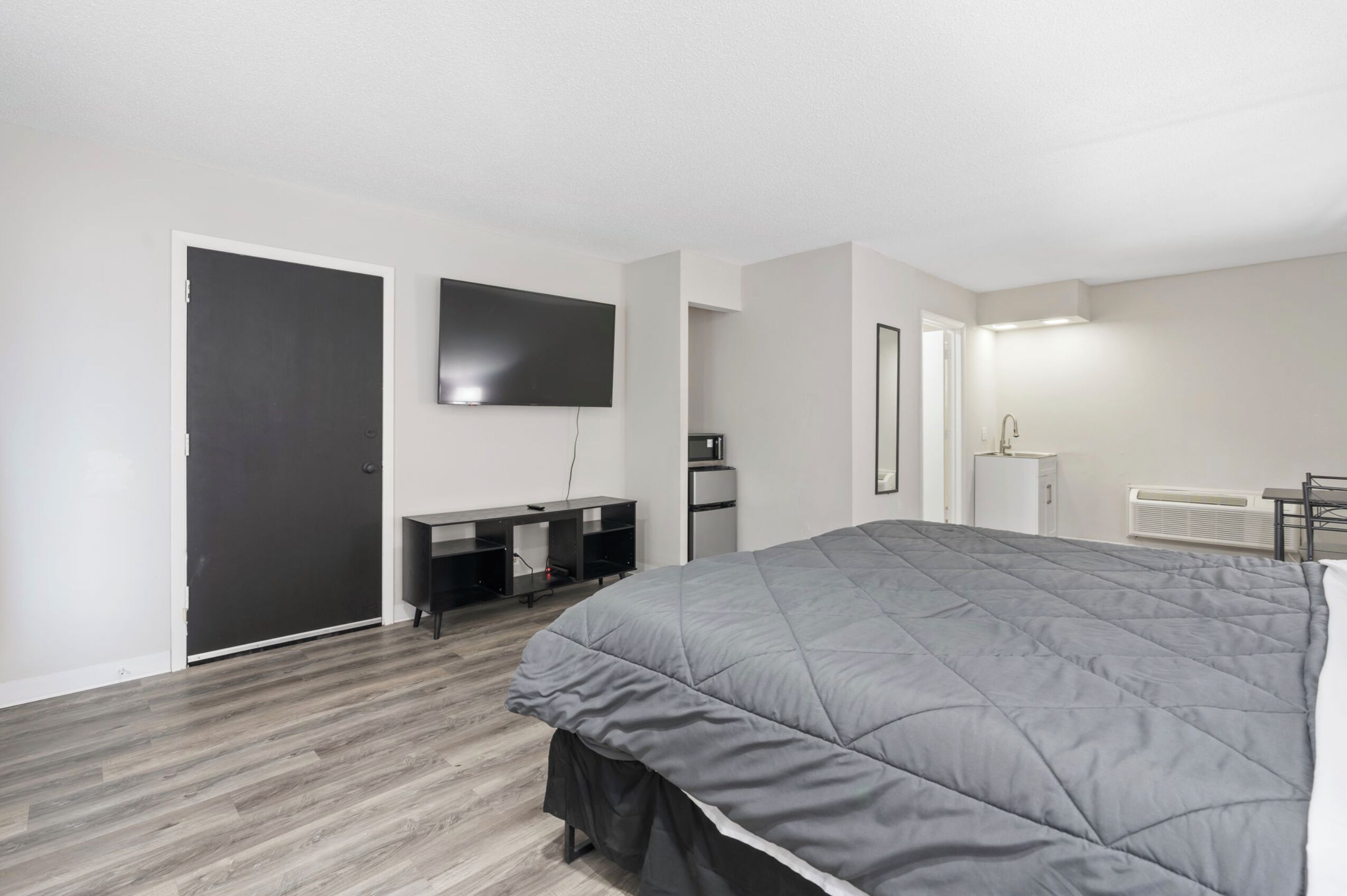 A modern bedroom with a large bed, a flat-screen TV, a desk, and a wardrobe.