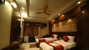 A hotel room with two beds, a TV, a ceiling fan, and a large window with curtains. - Hotel Orion  (Bhadrak)