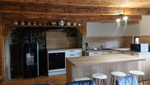 Eine rustikale Küche mit Steinwand, Holzschränken, einem schwarzen Kühlschrank, einer Mikrowelle und einer Bar mit Hockern.