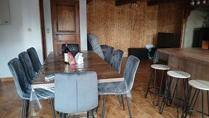 Ein Essbereich mit Holztisch und -stühlen, eine Küchenzeile mit Holzverkleidung und einer Arbeitsplatte sowie ein Fliesenboden.